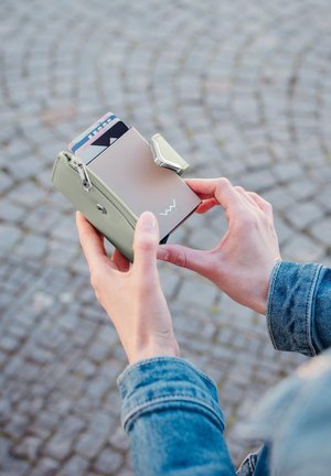 Mint green wallet with a silver pull tab, holding several cards. Smooth leather material, compact rectangular shape, zipper closure.