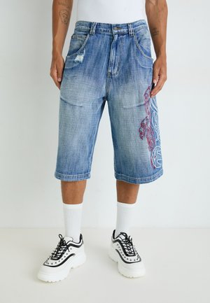 Denim šorti ar gaiši zilu mazgāšanu, ar nolietotiem pleķiem un sarkanu sarežģītu izšuvumu kreisajā pusē. Apvienoti ar masīviem melniem kedām.