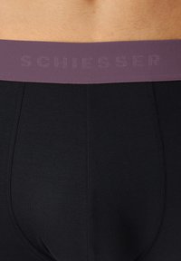 Boxer corto nero con una cintura texture viola che presenta il nome del marchio "SCHIESSER" in un colore a contrasto. Tessuto liscio e aderente.