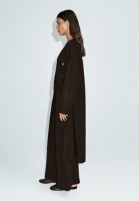 Haut à manches longues en tricot marron et pantalon large assorti, présentant une coupe horizontale et une coupe ample. Des chaussures plates foncées complètent le look.