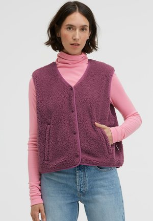 Fleece vest in purple, featuring a textured surface, V-neckline, front button closure, and side pockets, worn over a pink long-sleeve top.