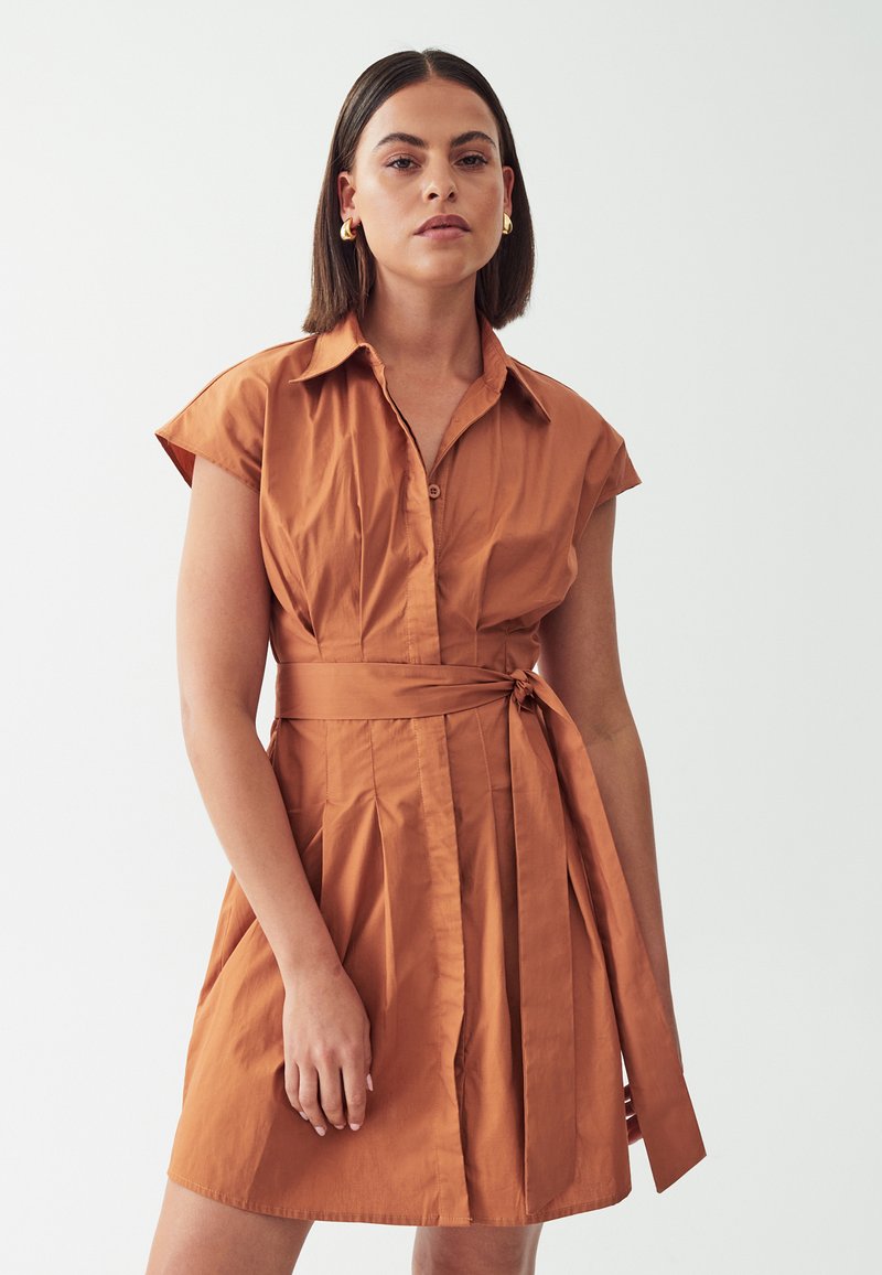 Rustfarbenes Hemdkleid mit kurzen, angeschnittenen Ärmeln, durchgehender Knopfleiste und gebundenem Taillendetail; mit plissierter Gestaltung. Glatter, leichter Stoff.