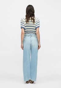 Suéter de punto con rayas horizontales azules y blancas y mangas cortas abullonadas, combinado con jeans de pierna ancha de tiro alto en azul claro y zapatos con estampado de leopardo.