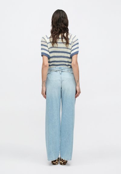 Πλεκτό πουλόβερ με οριζόντιες ρίγες σε μπλε και λευκό και κοντά φουσκωτά μανίκια, σε συνδυασμό με ψηλόμεσα, ανοιχτό μπλε τζιν παντελόνια με φαρδιά μπατζάκια και παπούτσια με λεοπάρ σχέδιο.