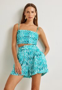 Top corto texturizado en turquesa y blanco con tirantes finos, combinado con pantalones cortos de patrón a juego que cuentan con una cintura ceñida y un corte relajado.