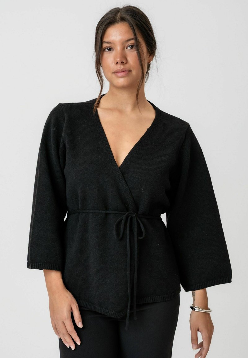 Pulover negru în stil tip înfășurare, din țesătură tricotată, având un decolteu adânc în V, mâneci largi și talie cu cordon. Finisaj texturat și detaliu la tiv.