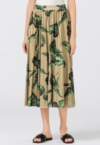 Plisserad midikjol i en beige tyg med stora gröna bladmönster. Har en elastisk midja och faller nedanför knäet. Svarta sandaler.