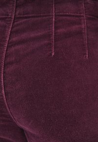 Bordowy materiał sztruksowy o drobnej fakturze, z detalami stębnowania i dopasowaną sylwetką zaprojektowaną z myślą o komforcie.