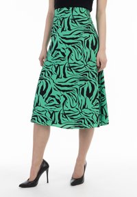 Groene midi-jurk met een zwart abstract patroon, gemaakt van lichtgewicht stof. Gepaard met zwarte hoge hakken.