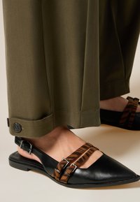 Zwarte leren slingback-schoen met een spitse neus, voorzien van bruine gestreepte banden en zilveren gespen; gedragen met olijfgroene broek.