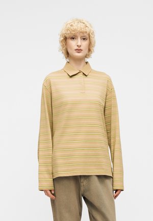 Person with curly blonde hair wearing a beige long-sleeve polo shirt with thin horizontal stripes and loose beige pants.