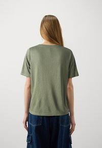 T-shirt en coton vert olive à manches courtes et à encolure ronde, porté avec un short en denim bleu foncé présentant des poches cargo.