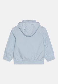 Ljusblå huva-jacka med elastiska ärmslut och midja. Har präglingen "HILFIGER" på kragen. Slät, lätt tyg.
