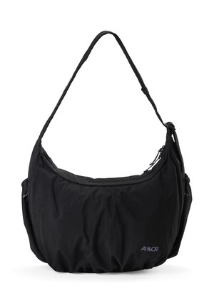 Schwarze Schultertasche aus Stoff mit verstellbarem Riemen, Reißverschluss, Seitentaschen und kleinem "AEVOR"-Logo vorne unten rechts.