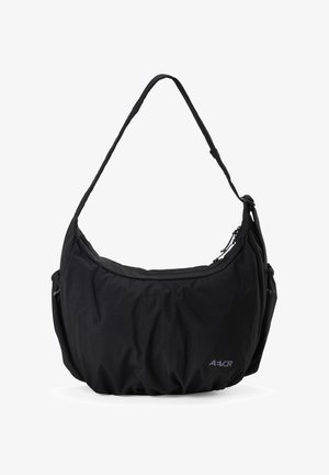 Sac d'épaule en tissu noir avec sangle réglable, fermeture éclair, poches latérales et petit logo "AEVOR" en bas à droite à l'avant.