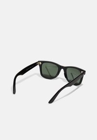 Gafas de sol negras con lentes verdes, diseño de montura cuadrada, acabado brillante y acentos metálicos en las bisagras. Las patas son lisas y rectas.