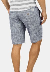 Shorts albastre cu un model, fabricate dintr-un material ușor. Prezintă două buzunare pe spate cu închidere prin buton și o croială lejeră, care ajunge până la jumătatea coapsei.