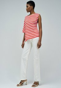 Top a rayas rojas y blancas con una manga corta; combinado con pantalones anchos blancos y sandalias de tacón alto beige con tiras. Textura suave.