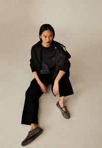 Schwarzer Sweatshirt mit strukturierten Akzenten und grauen Verzierungen, kombiniert mit schwarzen weitem Beinkleid und gepunkteten Schuhen mit Riemen.