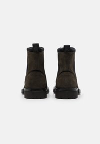 Bottines noires et vert olives avec un cuir lisse sur le dessus, des panneaux en daim texturé et une semelle en caoutchouc épaisse avec une languette.