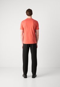 Tricou scurt, de culoare corai, cu mânecă scurtă și guler rotund, combinat cu o pereche de pantaloni negri, lejere. Design simplu, textură moale, detalii minime.