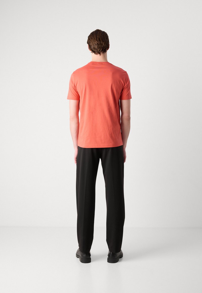 Korallefarbenes T-Shirt mit kurzen Ärmeln und Rundhalsausschnitt, kombiniert mit schwarzen, lockeren Hosen. Einfaches Design, weicher Stoff, minimale Details.