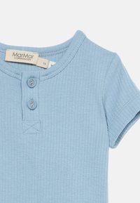 Γαλάζιο ριμπ κοντομάνικο παιδικό πουκάμισο με δύο κουμπιά μπροστά και ετικέτα της μάρκας MarMar Copenhagen.