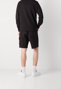 Černá mikina a kraťasy z měkké látky; kraťasy mají boční kapsu; nošeno s bílými teniskami a kotníkovými ponožkami.