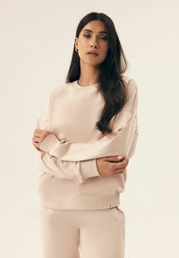 Jasnoróżowy, luźny sweatshirt z ribbowanymi mankietami i dolnym wykończeniem. Miękka tekstura, okrągły dekolt i przeszycia na ramionach.