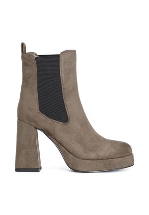 Bottines en daim marron avec une forme carrée, semelle en caoutchouc et talon bloc haut. Équipées de panneaux latéraux élastiques pour un enfilage facile.