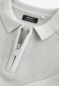 Pull-over en tricot texturé gris clair, avec un col zippé et une étiquette noire "NEXT". Présente un détail de fermeture éclair en argent lisse.
