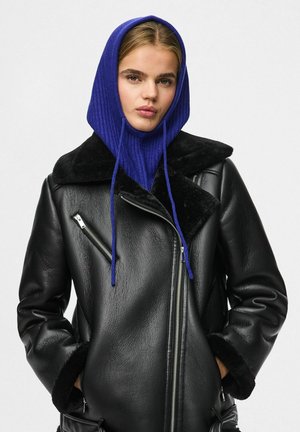 Musta nahkatakki tekoturkiskauluksella, jossa on vetoketjusuljin ja sivutaskut, yhdistettynä siniseen resorihuppuun nyörillä.