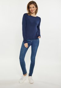 Navyblaues Langarmshirt mit rundem Halsausschnitt, kombiniert mit blauen Skinny Jeans und weißen Sneakers. Glattes, leichtes Material mit lockerer Passform.