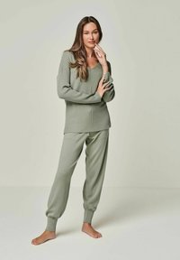 Hellgrünes, geripptes Loungewear-Set mit einem locker sitzenden Pullover mit V-Ausschnitt und tapering Hosen mit elastischen Bündchen. Der Stoff wirkt weich.