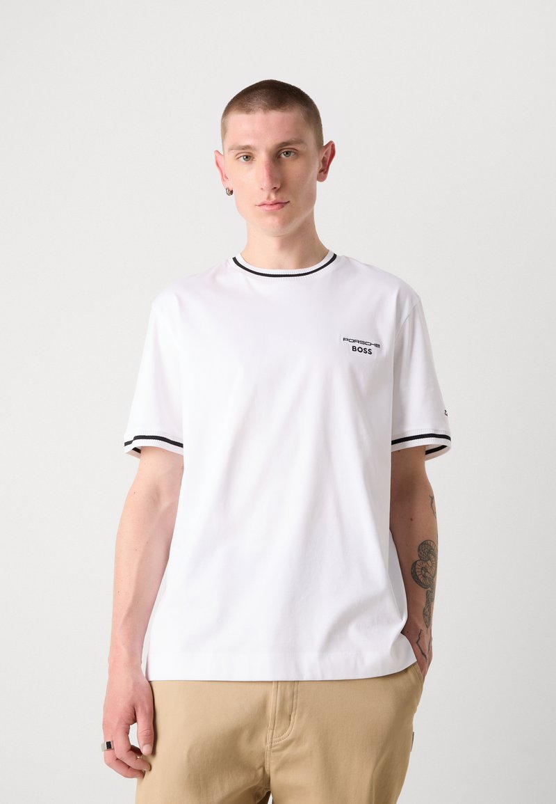 T-shirt bianca a maniche corte con rifiniture nere sul colletto e sulle maniche, con un piccolo logo sul lato sinistro del petto. Vestibilità casual, materiale in cotone.