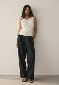 White draped top with a smooth finish, paired with high-waisted black wide-leg trousers. Model wears strappy black sandals.