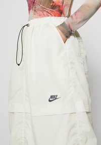 Fehér Nike rövidnadrág, rugalmas derékpánttal és fekete húzózsinórral. Két oldalsó zsebbel rendelkezik, és az elején egy nyomtatott logó található. Sima textúrájú.