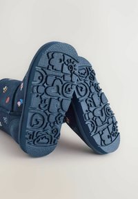 Námornícky modrá obuv s textúrovanou gumovou podrážkou s vzorom tvarov, vrátane srdiečok a kvetov, a mäkkým horným materiálom.