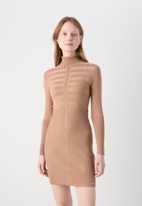 Robe en tricot beige à col montant, présentant des rayures verticales sur le haut et une texture côtelée sur la jupe. Design ajusté avec des manches longues.