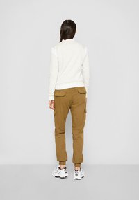 Jasno beżowa bluza z białymi akcentami, w połączeniu z beżowymi spodniami cargo z bocznymi kieszeniami i elastycznymi mankietami, noszona z białymi sneakersami.