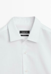 Weißes Baumwollhemd mit glatter Textur, ausgestattet mit Vorderknöpfen und zwei Etiketten: "Massimo Dutti" und "Hergestellt in der Türkei."