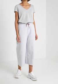 Helles graues Baumwoll-T-Shirt mit V-Ausschnitt und kurzen Ärmeln, kombiniert mit lockeren, hellgrauen Sweatpants, die über einen elastischen Bund und eine Kordel verfügen.