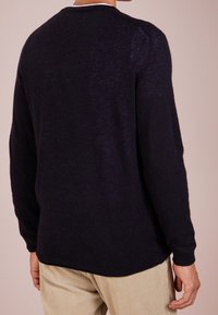 Marineblauer gestrickter Pullover mit langen Ärmeln, rundem Halsausschnitt, geripptem Saum und glatter Textur. Getragen über hellen Cordhosen.