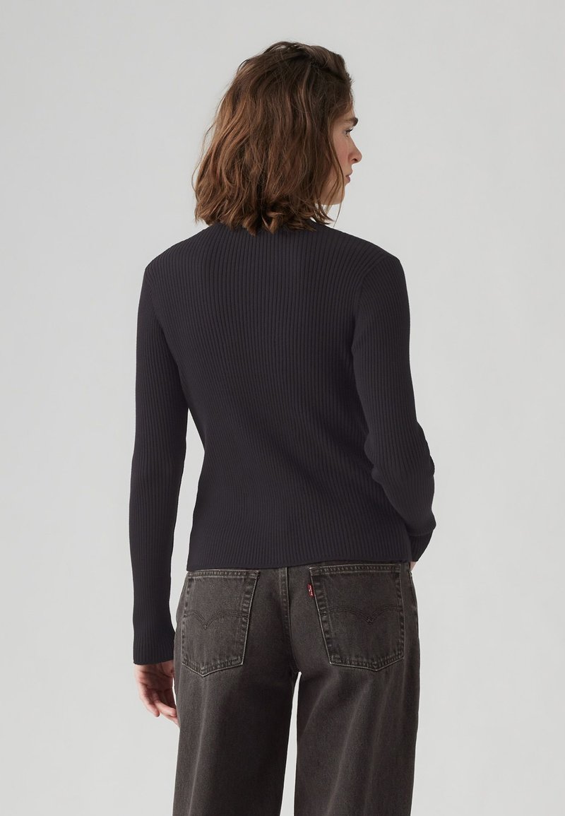 Marineblaues, geripptes Langarmoberteil mit taillierter Silhouette. Ausgestattet mit einem hohen Ausschnitt und glatter Textur, kombiniert mit dunkelgrauen Weitbeinhosen.