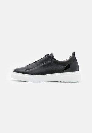 Sort lav-top læder sneakers med hvid gummisål og snørelukning foran, set fra siden på en ensfarvet hvid baggrund.