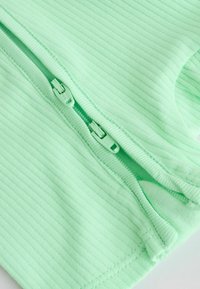 Gros plan sur un tissu côtelé vert clair avec une fermeture éclair assortie verte partiellement ouverte le long de la couture.