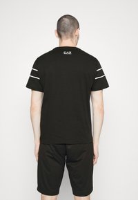 Svart bomullströja med korta ärmar, prydd med vita ränder på axlarna och en logotyp på övre ryggen. Matchad med svarta shorts.