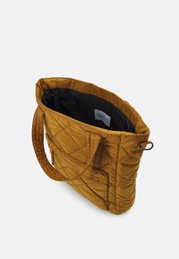 Bolsa tote de mostarda acolchoada com duas alças de tecido, topo aberto e um interior preto com um rótulo e um bolso com fecho.