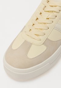Beżowe sneakersy z gładkiej skóry z teksturalnymi akcentami, płaskimi sznurowadłami i białą gumową podeszwą. Okrągły czubek i przeszycia.