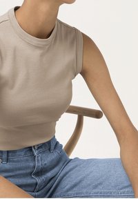 Light beige sleeveless top with a high neckline, made of soft cotton, paired with high-waisted blue denim jeans. Smooth texture, fitted design.